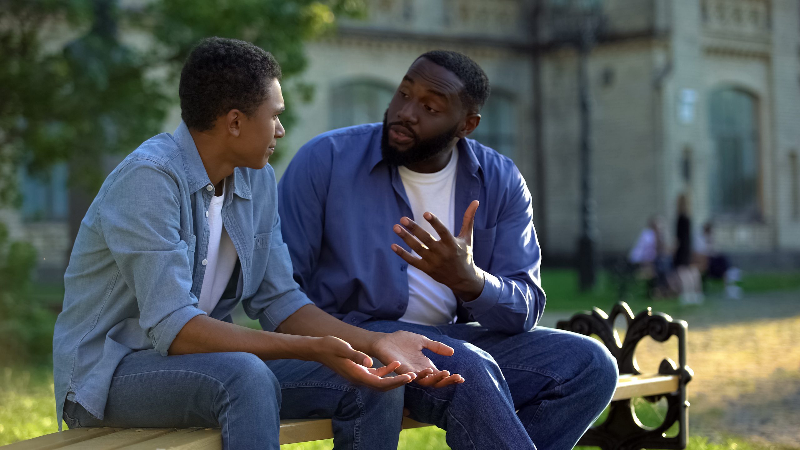 Father arguing teenage son sitting on campus bench, puberty age